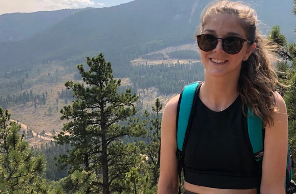 A young woman wearing sunglasses poses on the edge of a cliff.